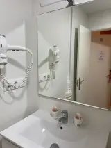 Lavabo del baño con espejo grande y secador de pelo de pared, con vasos de aseo sobre la encimera